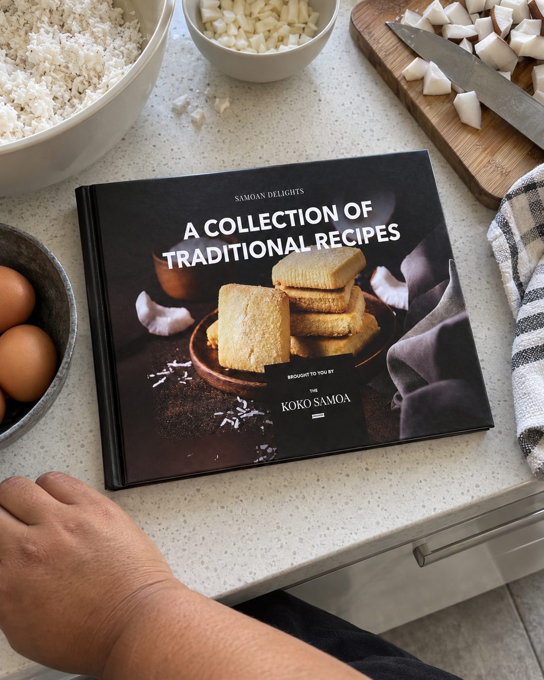 Cookbook in the 12 Samoan Recipes Vol 1 print, closed on a kitchen bench while cooking.